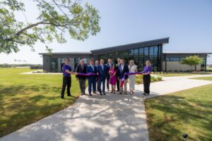 A modern building behind a group of people cutting a purple ribbon.