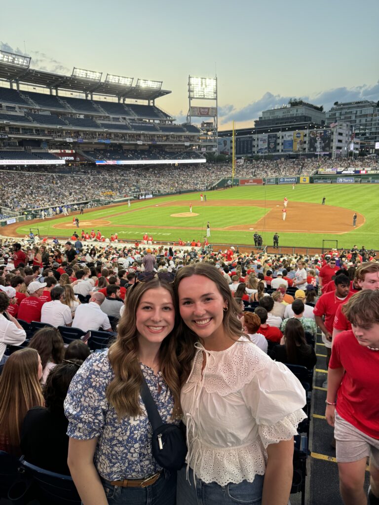 Zoë Meeks, who is completing an internship at the National Cotton Council, stands next to another young woman at a baseball game. 