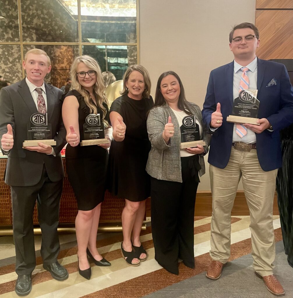 Two women and three men stand in a line while four of them hold glass trophies from the American Meat Science Association. All are holding their thumbs up in front of them.