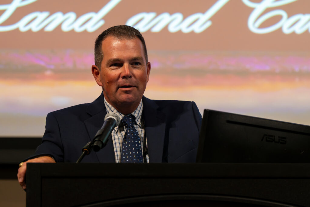 A man with a suit and tie, Jason Cleere, stands behind a podium and opens the Texas A&M Beef Cattle Short Course.