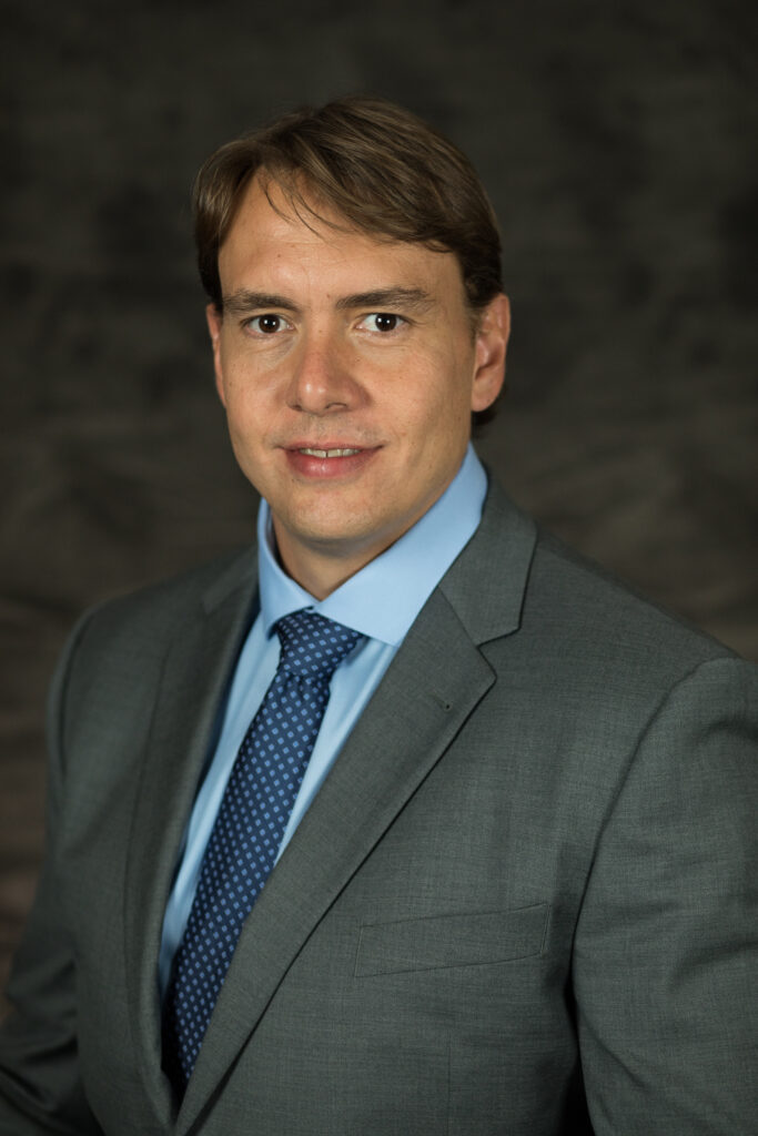 A man in a dark suit with a blue shirt and tie, Reinaldo Cooke, Ph.D., Burkhart Endowed Professor for Beef Cattle Research in the Department of Animal Science