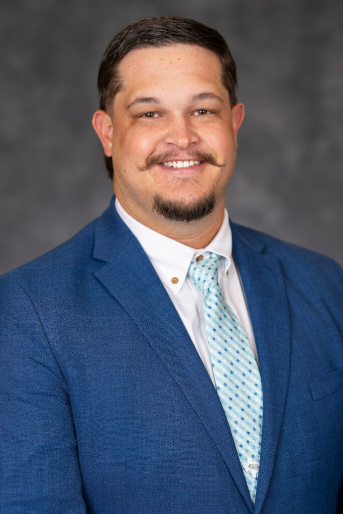 Smiling man with a mustache and blue jacket with light blue tie. New agent