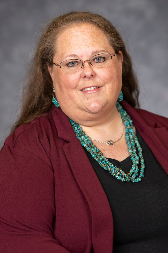 A smiling female agent in maroon jacket over black blouse with heavy turquoise necklace and earrings