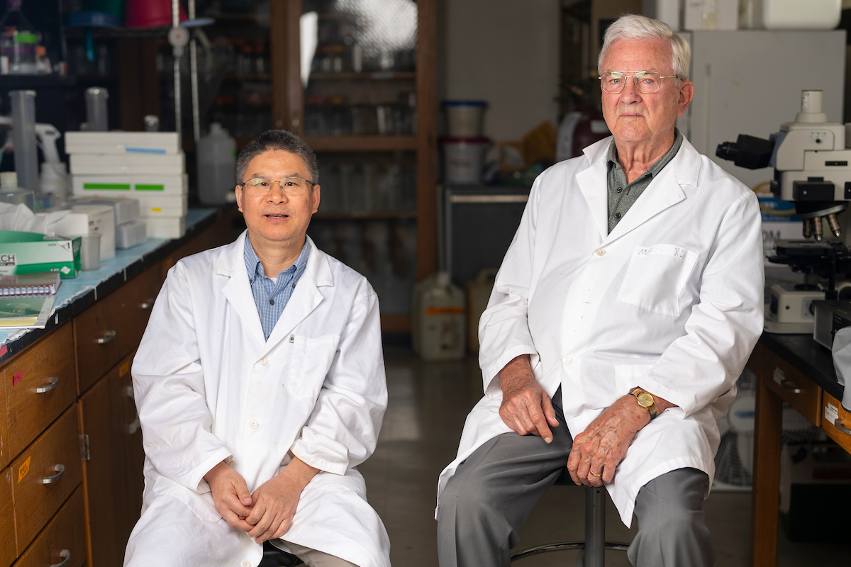 two animal science researchers, Guoyao Wu and Fuller Bazer, sit in a lab setting with their white coats on