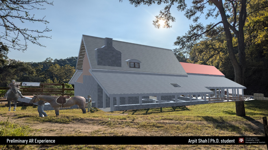 In an opening in the woods, there is a grey barn and horses that are generated through augmented reality technology. The sun is shining with a blue sky. 