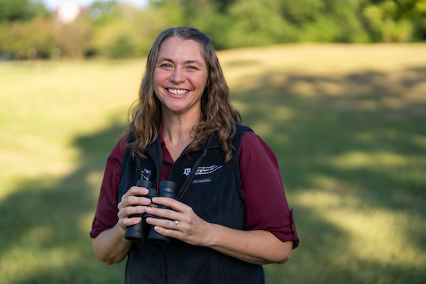 A woman outdoors holding binoculars and smiling. 