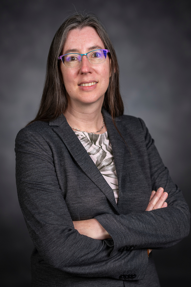 Portrait of Ann Wehman sitting with arms crossed in front of a gray background